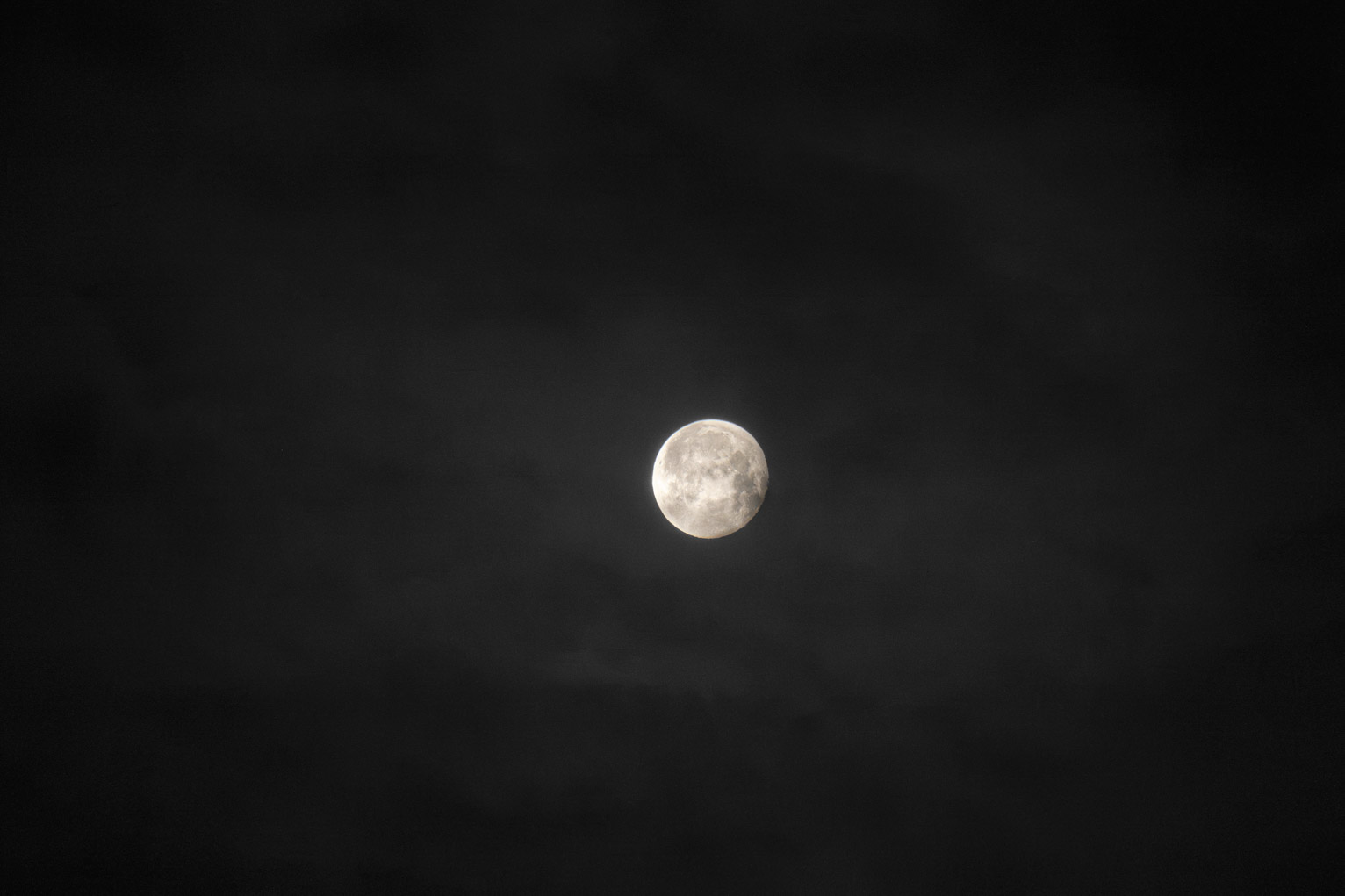 A close to full moon lights some thin clouds about